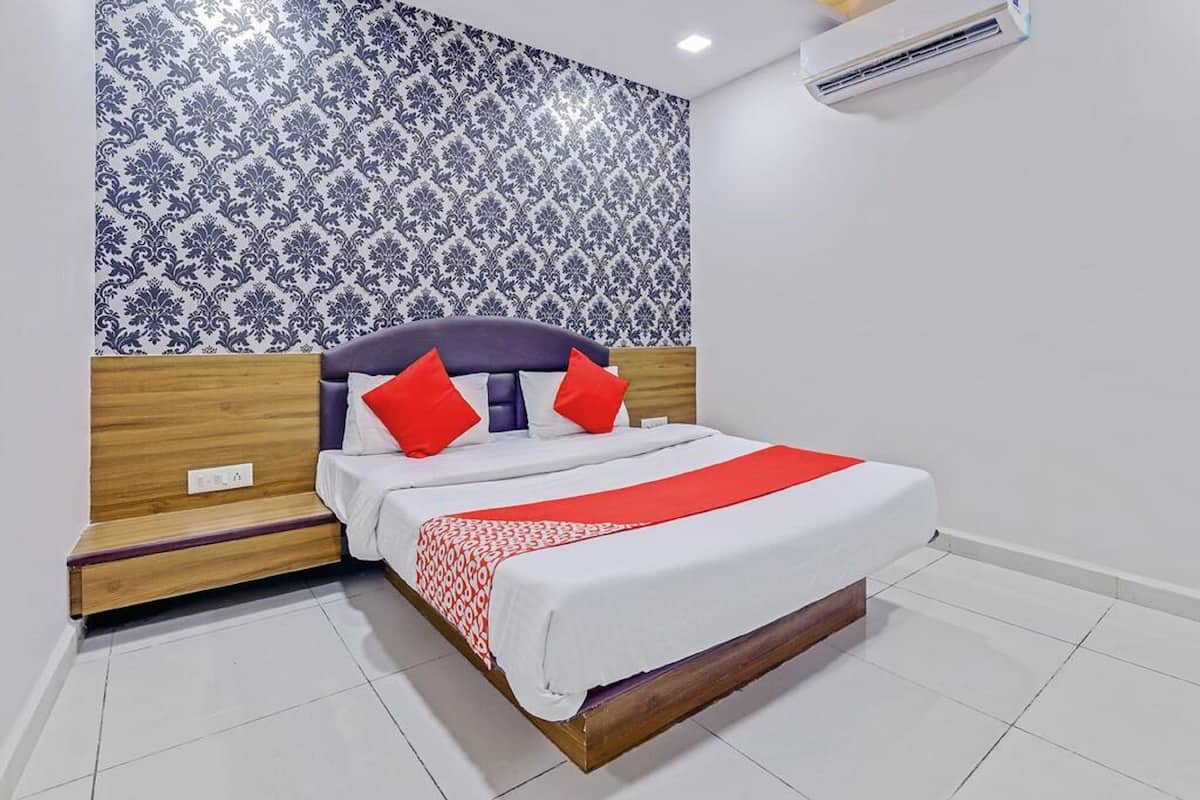 A neatly made bed with a wooden headboard, a red and white patterned bedspread, and two red pillows.