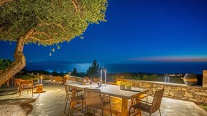 Un área de comedor al aire libre con una mesa y sillas, un muro de piedra y vistas al mar de noche.
