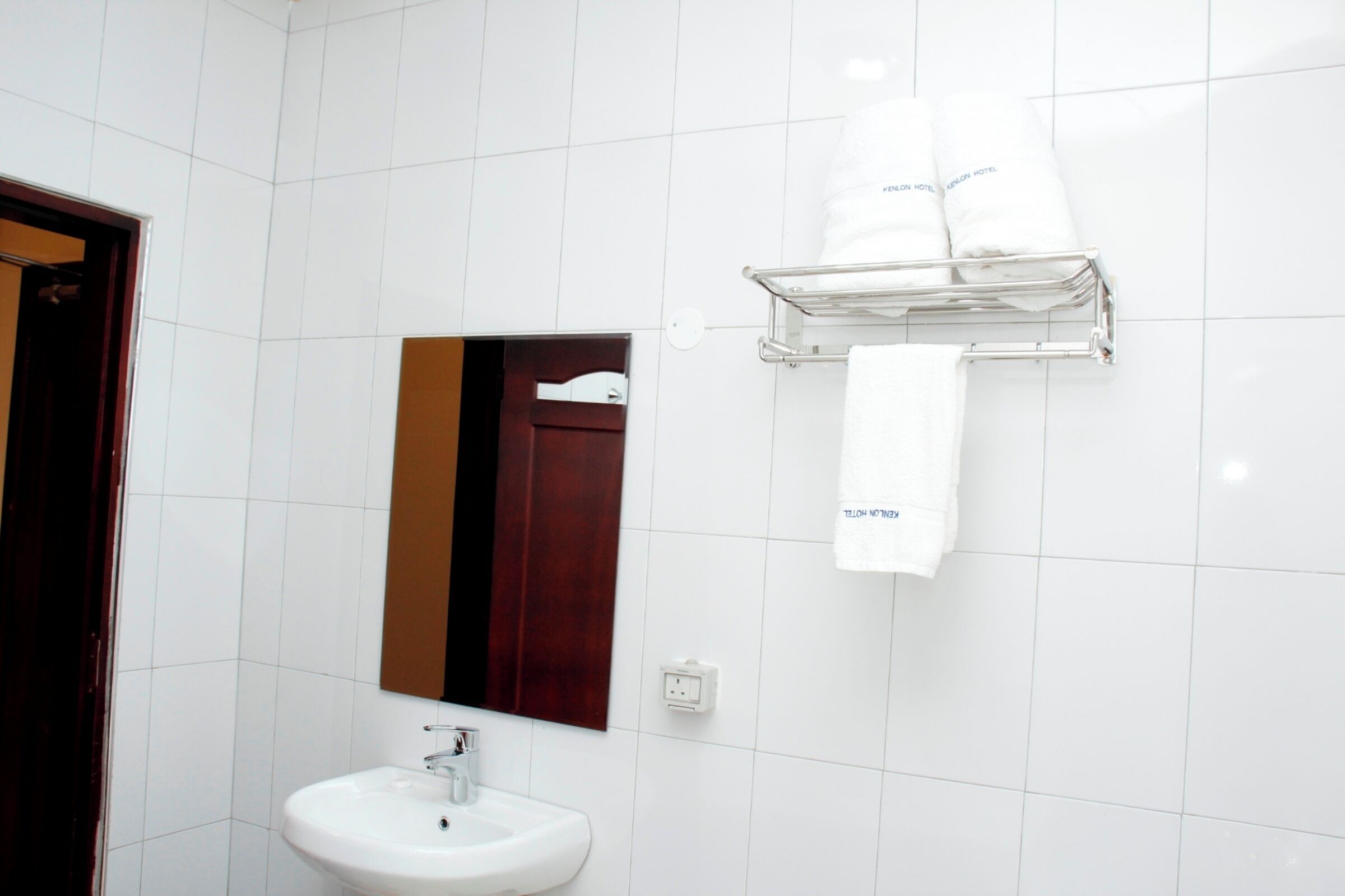 A bathroom with white tiles, a sink, a mirror, and a towel rack with towels.