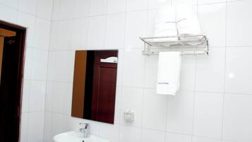 A bathroom with white tiles, a sink, a mirror, and a towel rack with towels.