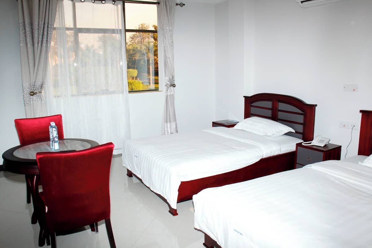 Habitación de hotel con dos camas, una mesita pequeña con una silla, una mesita de noche con un teléfono y una ventana con cortinas.
