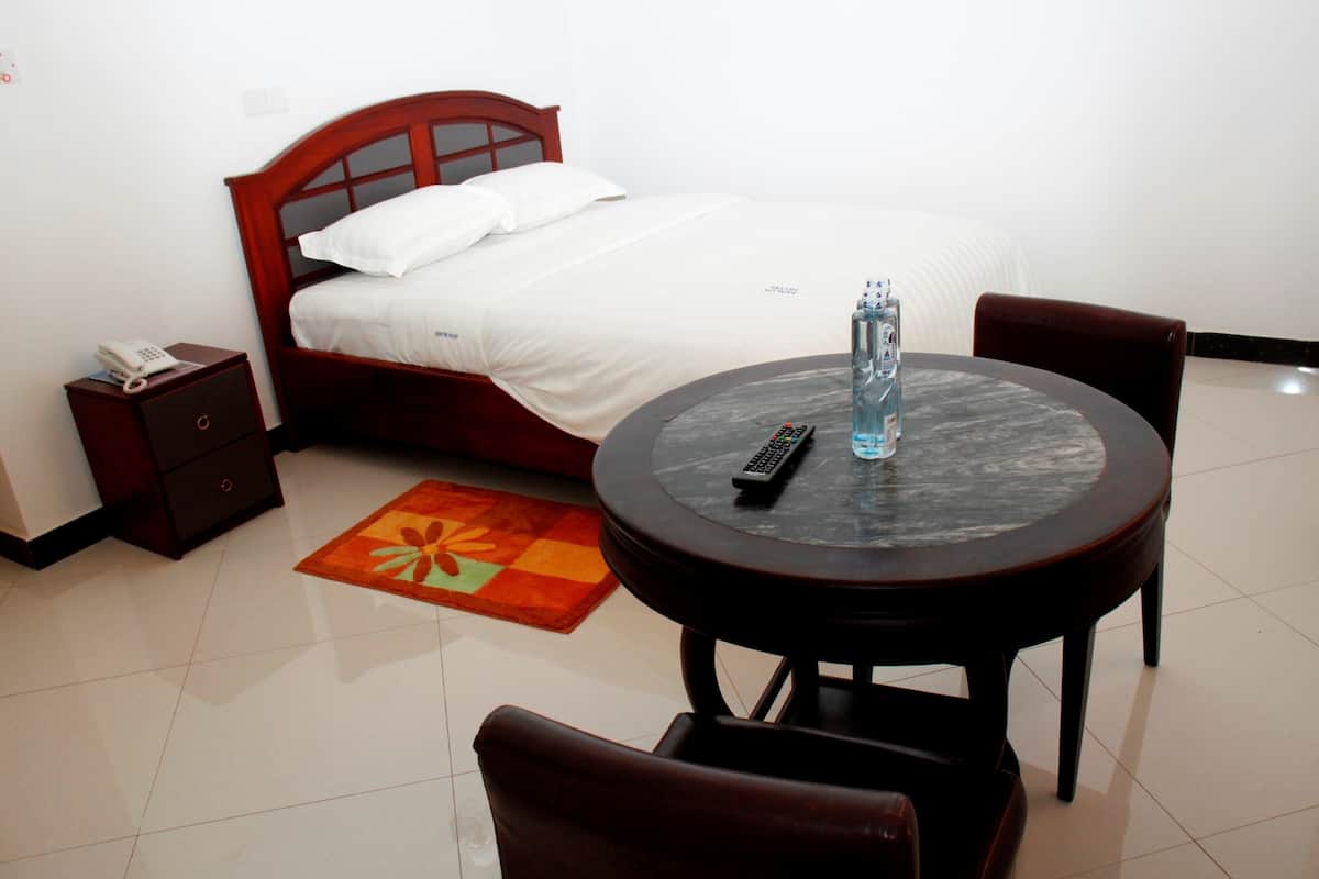 Habitación de hotel con cama, mesita de noche con teléfono, mesa redonda con control remoto y una silla.