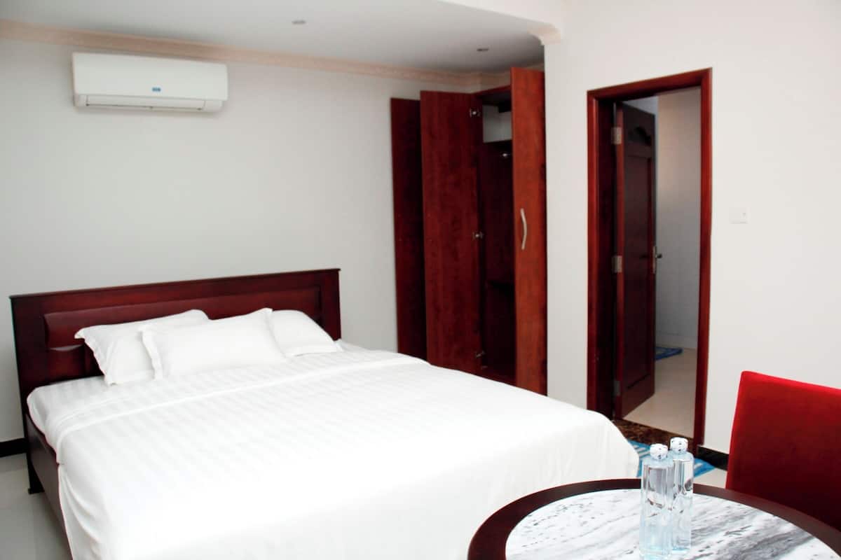Una habitación de hotel con una cama, una mesa redonda, una silla roja y un armario.