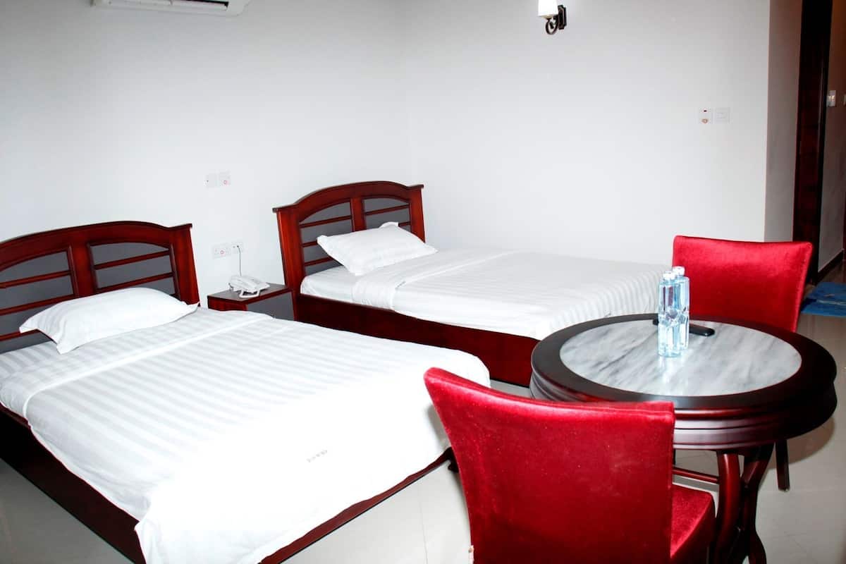 Habitación de hotel con dos camas individuales, una mesa redonda con una silla y una botella de agua sobre la mesa.