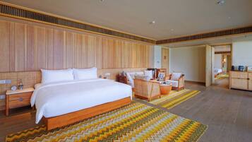 A hotel room with a large bed, a sitting area with a sofa and chairs, a wooden wardrobe, and a small table with a kettle.
