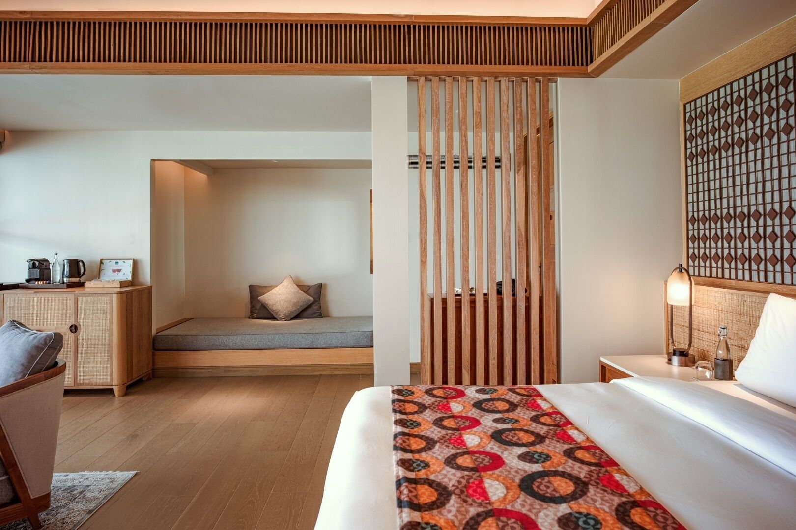 Una camera d'hotel con un letto, una zona salotto, un comodino e un pannello decorativo a parete.