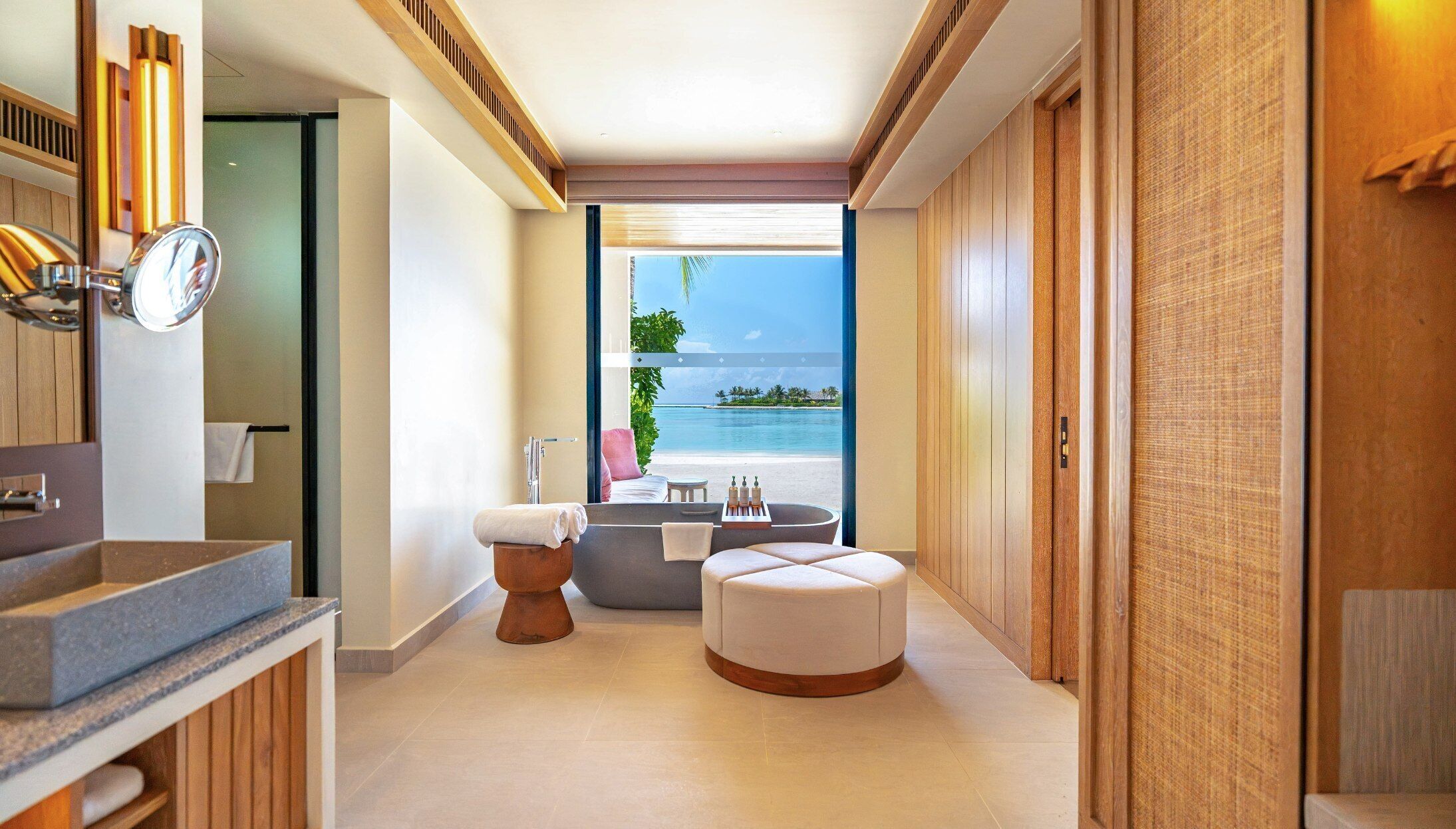 Un baño moderno con bañera, inodoro y tocador. Se ve la playa y el océano a través de un ventanal grande.