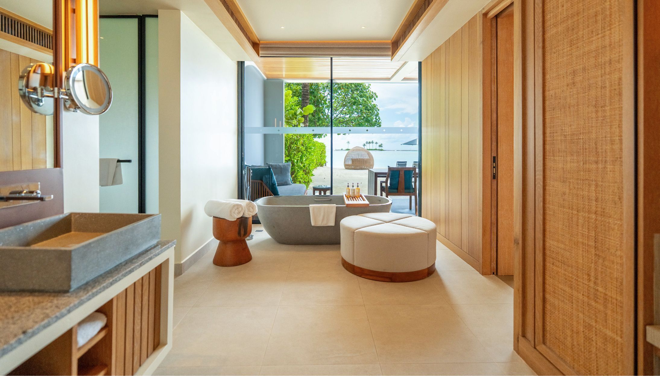 A modern bathroom with a large bathtub, a vanity with a mirror, and a view of the beach.