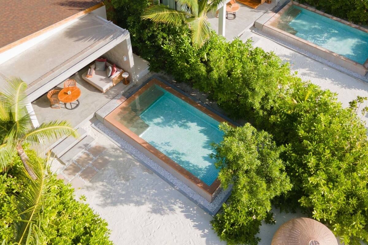 A rooftop pool area with multiple swimming pools, surrounded by lush greenery and palm trees.