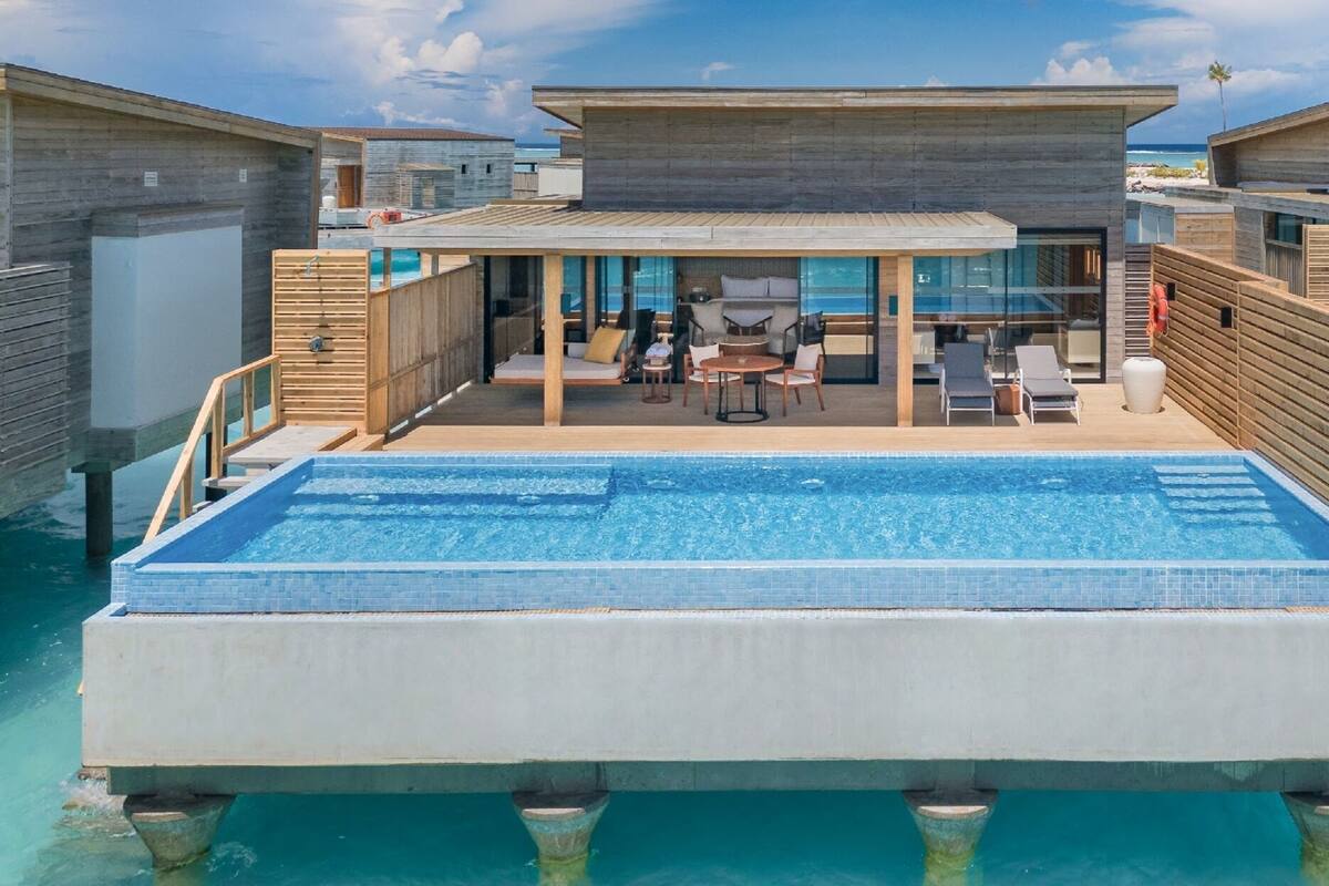 A modern resort with an infinity pool, wooden deck, and glass-enclosed lounge area.