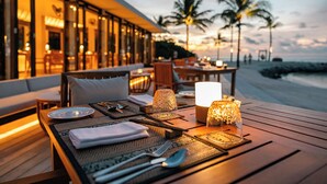 A table set for dining with a view of the beach and palm trees at dusk. - Kuda Villingili Maldives, Free Return Transfers 03 nights & above (Kuda Villingili)