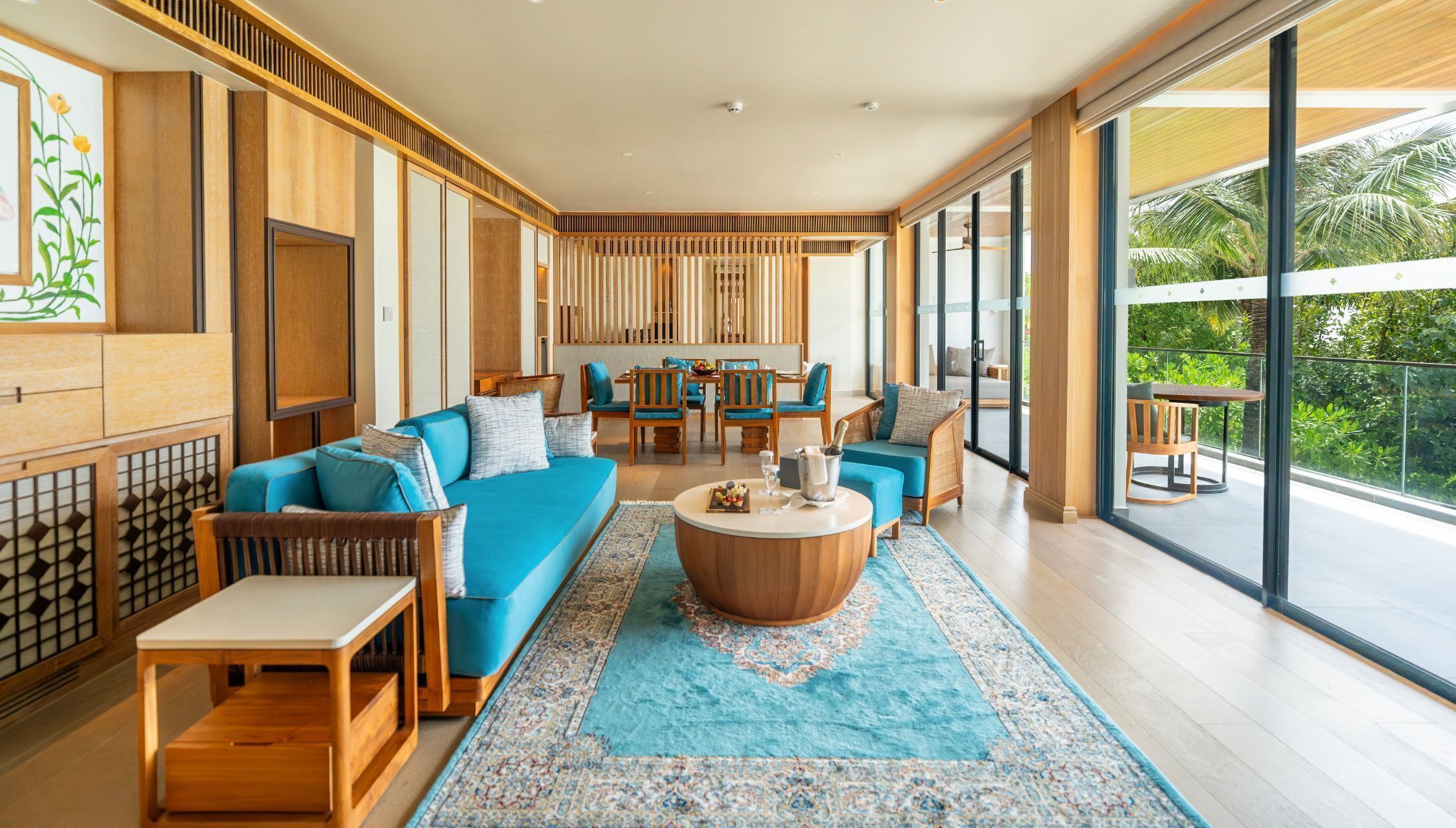 A modern living room with a blue sofa, wooden furniture, and a large window offering a view of greenery.