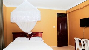 A hotel room with a bed, a white canopy, a TV mounted on the wall, and two white chairs. - Floral Hotel (Kampala)