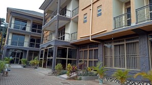 A multi-story building with balconies, large windows, and a paved entrance area with potted plants. - Floral Hotel (Kampala)
