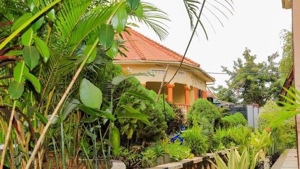 A house with a red-tiled roof, surrounded by lush greenery and potted plants. - Floral Hotel (Kampala)