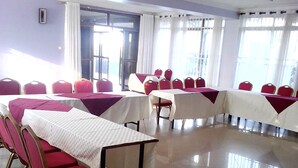 A conference room with rows of tables and chairs, large windows with curtains, and a tiled floor. - Floral Hotel (Kampala)
