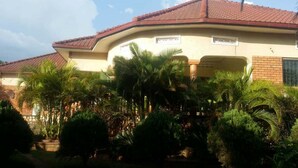 A house with a curved roof, a brick exterior, and a covered porch with palm trees. - Floral Hotel (Kampala)