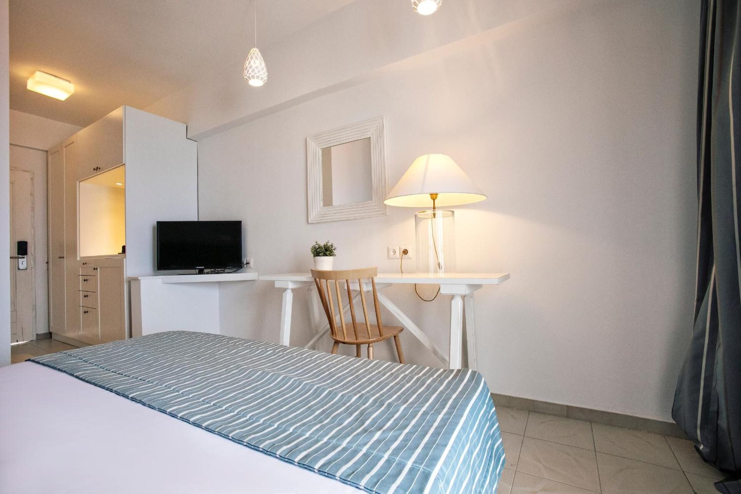Una habitación de hotel con cama, escritorio con lámpara, televisor y espejo.