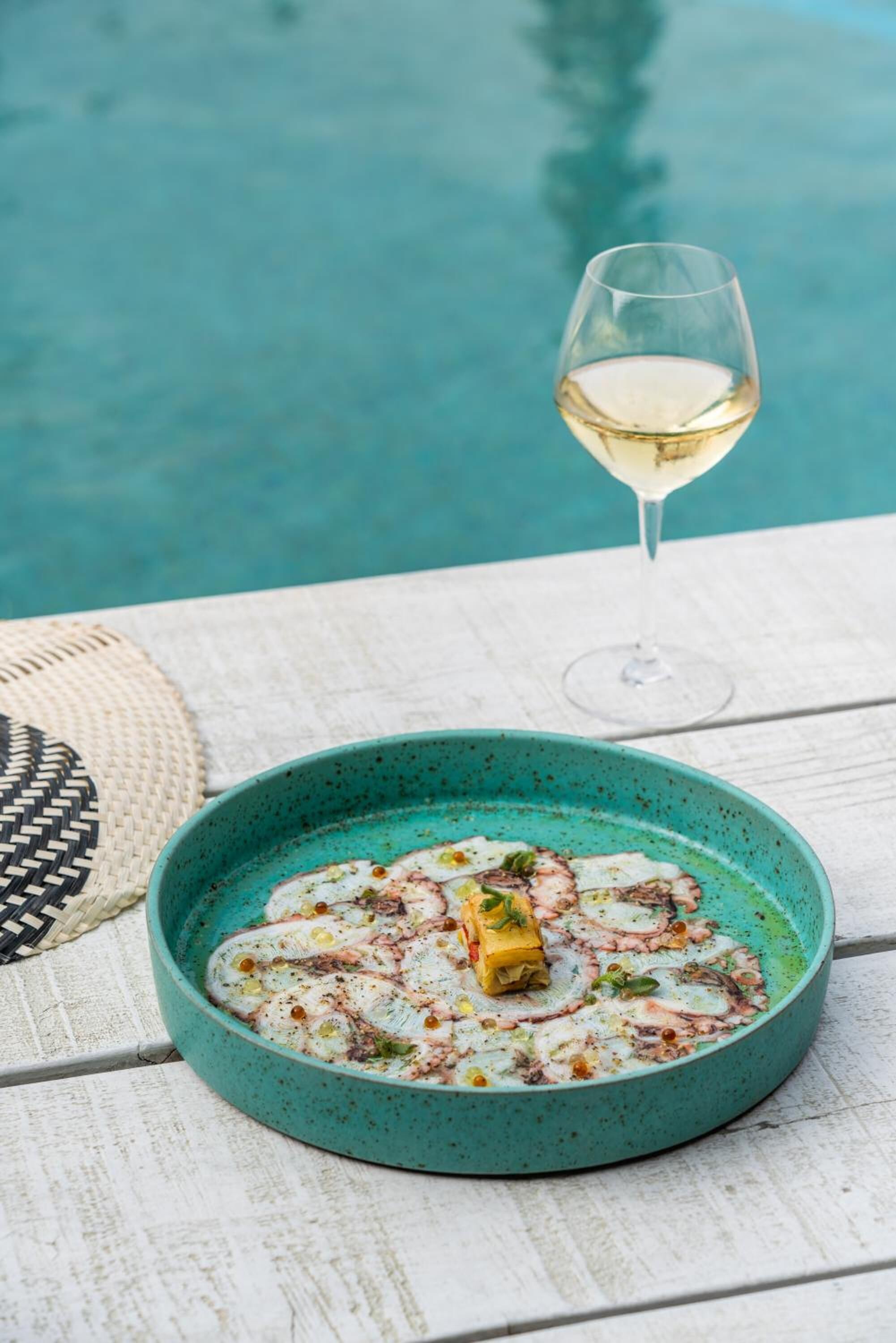 A turquoise bowl of seafood on a wooden table by a pool.