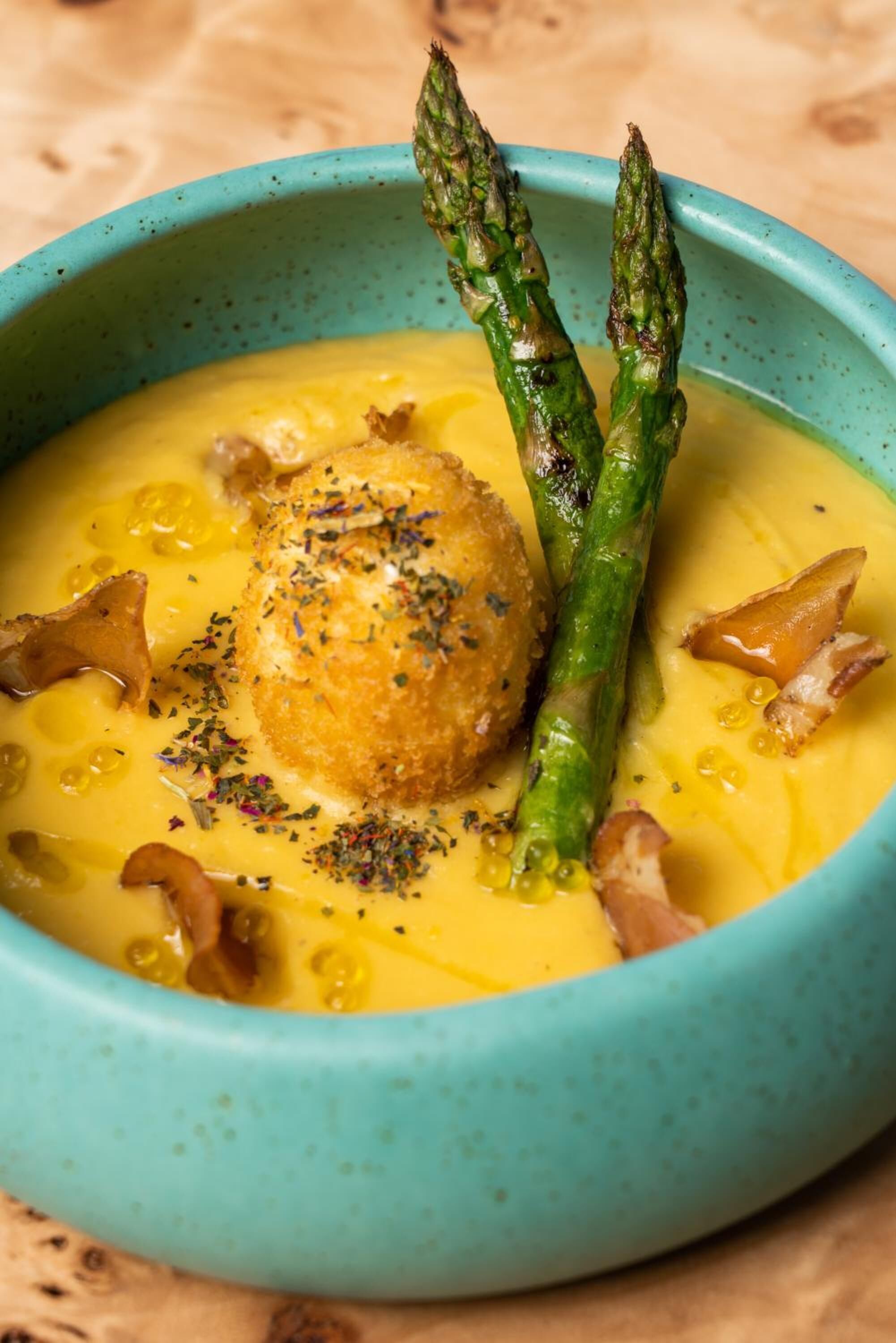 A bowl of soup with asparagus and a round breaded item, garnished with herbs.