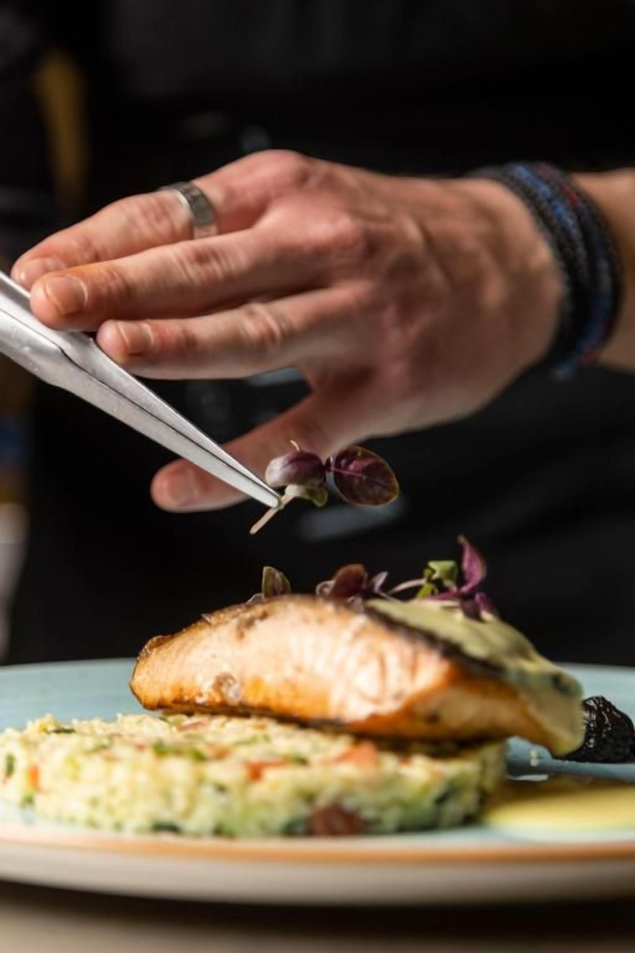 Iemand gebruikt een hulpmiddel om een gerecht te garneren met zalm en groenten.