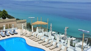 Zona de piscina con sillones y sombrillas, con vista a una gran extensión de agua y montañas distantes.