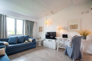 Un soggiorno moderno con un divano blu, una scrivania bianca, una televisione e una lampada.