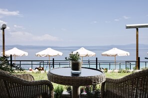 A round wicker table with a potted plant in the center, surrounded by wicker chairs, with white umbrellas and a view of the sea.