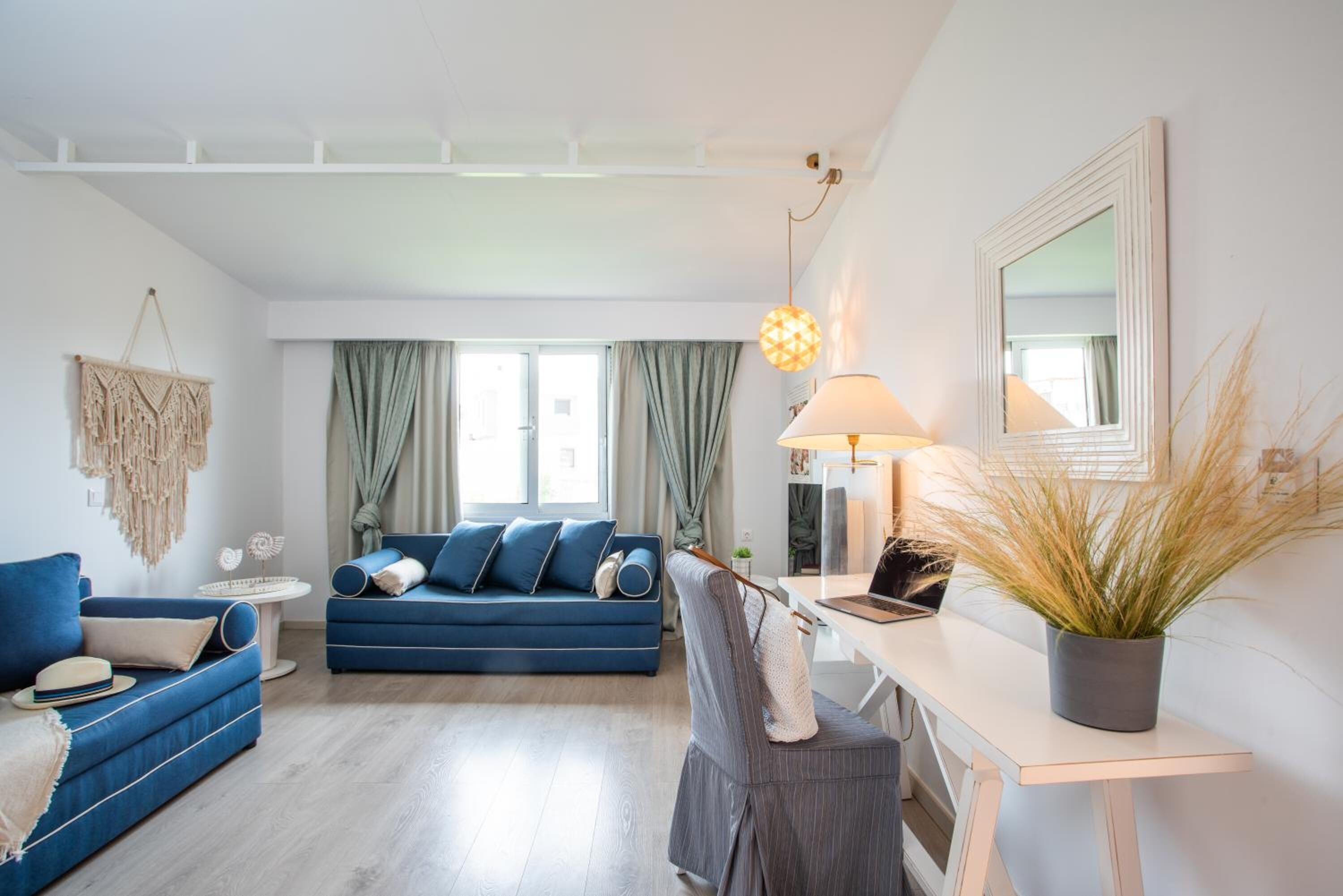 Uma sala de estar moderna com um sofá azul, uma poltrona cinza, uma escrivaninha branca e um abajur pendente.