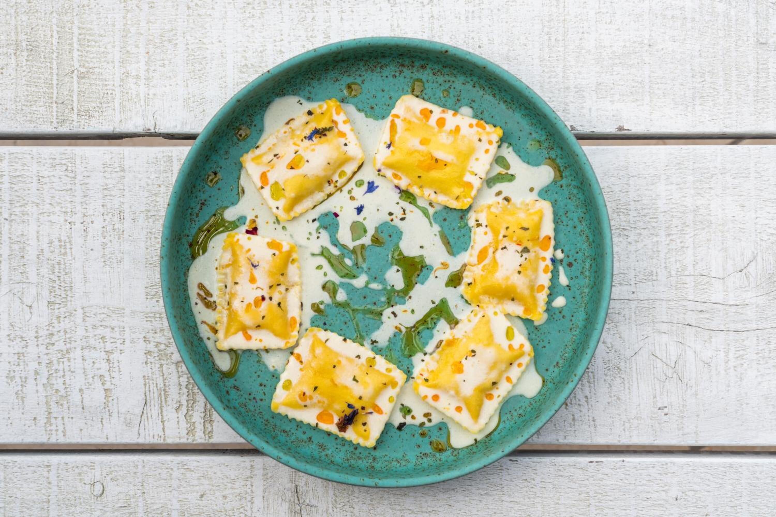 A plate of ravioli with a creamy sauce and herbs, on a rustic white wooden table.