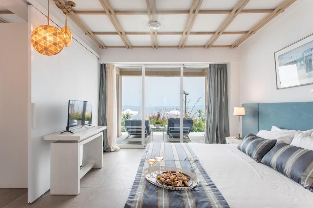 Ein Hotelzimmer mit Bett, Fernseher, Esstisch mit einer Serviertage und einem Balkon mit Stühlen.