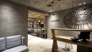 Una moderna zona de recepción con un escritorio de madera, un sofá gris y un cartel con la palabra 'WELCOME' en la pared.