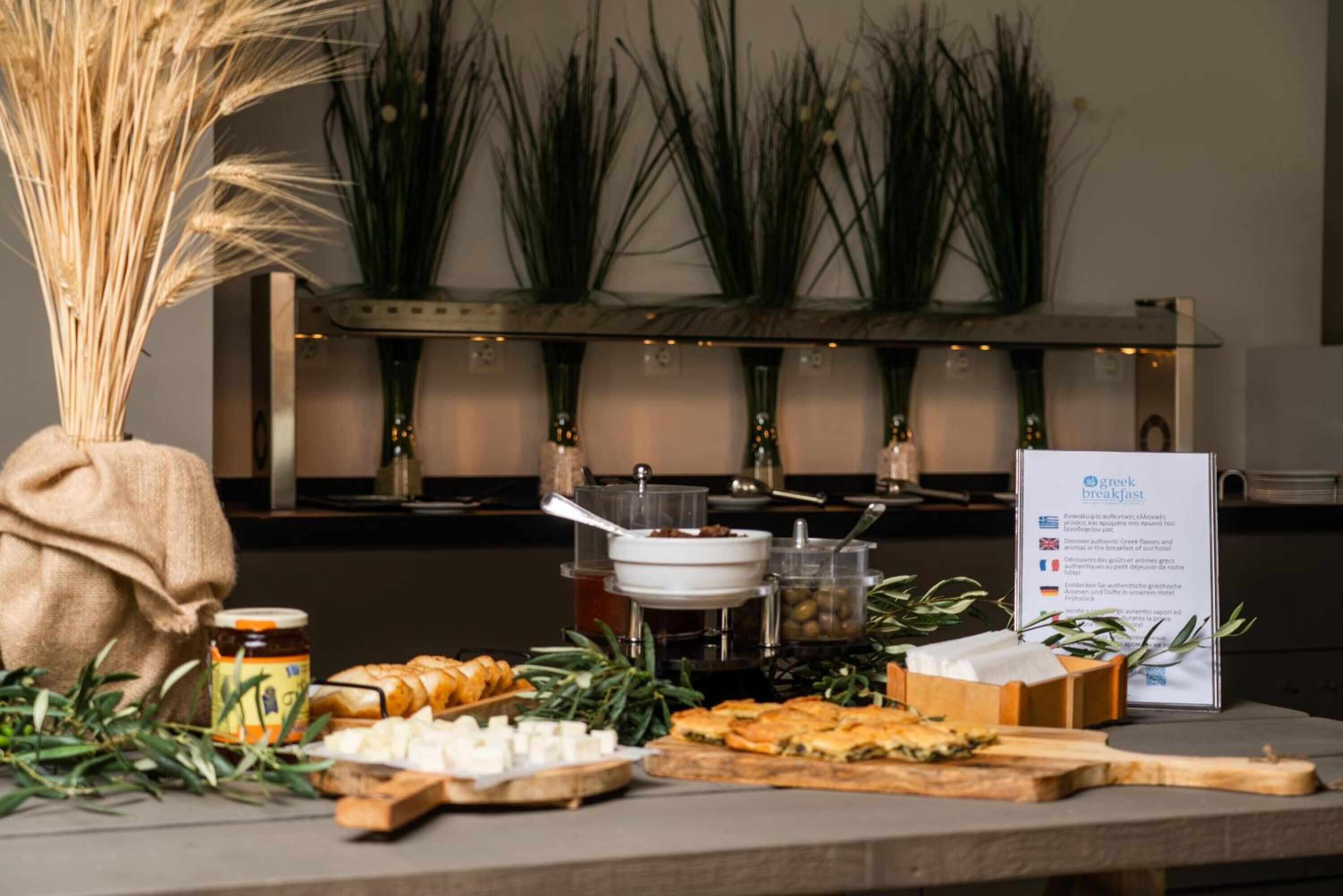 A breakfast buffet with various food items, a sign about breakfast, and decorative plants.