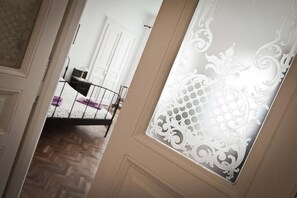Un pasillo con una puerta decorada y una cama con estructura metálica y una manta morada.