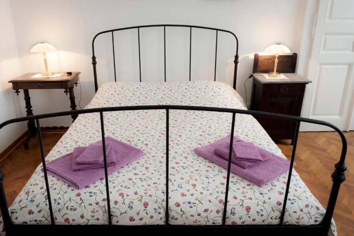 A single bed with a floral-patterned mattress, two purple towels, and two bedside tables with lamps.