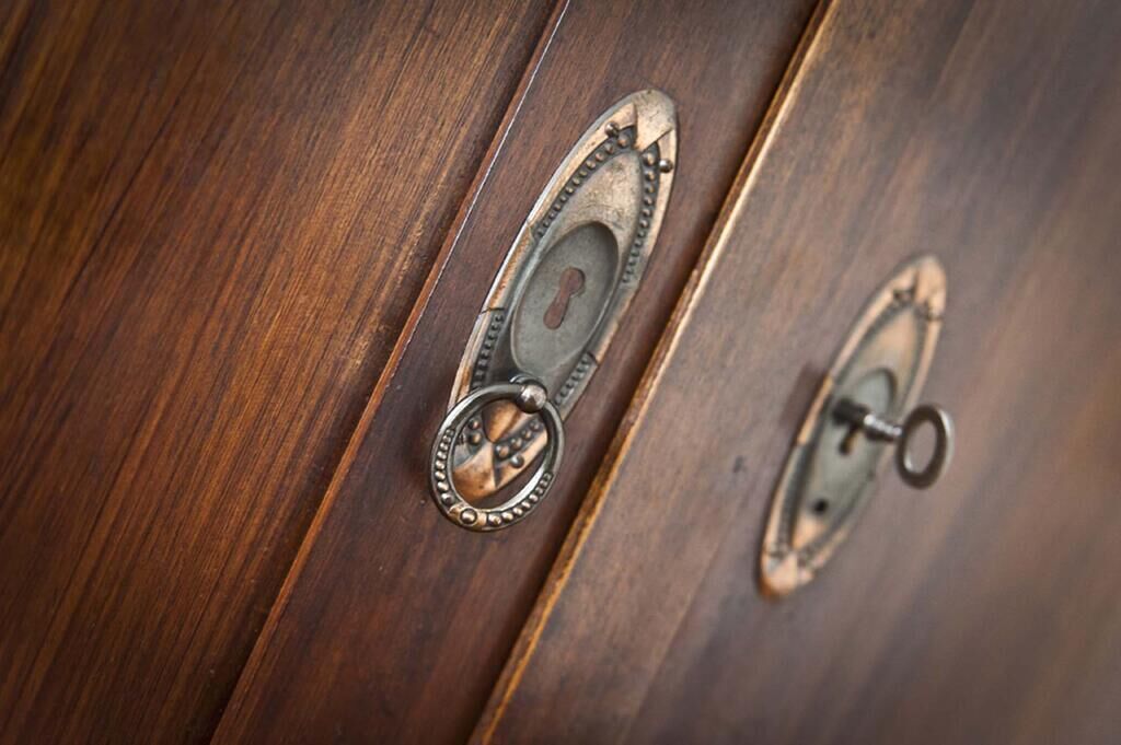 A close-up of a wooden surface with two metallic handles, one of which is open revealing a keyhole.