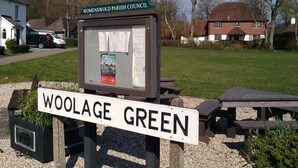 Un panneau indiquant l’entrée de Woolage Green, avec un panneau d’affichage au premier plan.