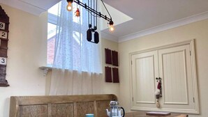 Un coin repas avec une table en bois, des chaises, une cafetière et une fenêtre avec des rideaux.