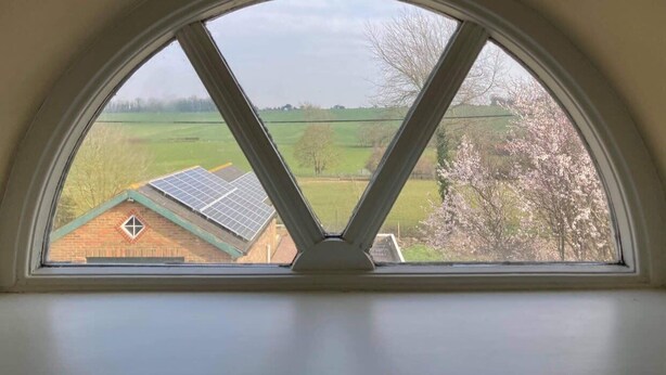 Une lucarne offrant une vue sur un champ verdoyant et un bâtiment équipé de panneaux solaires.
