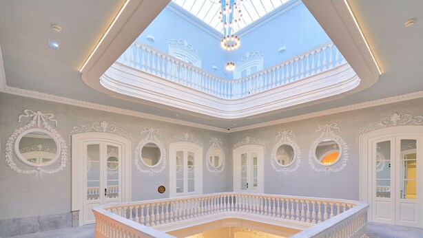Interior imponente com um espaço aberto central, grades brancas ornamentadas e um skylight.