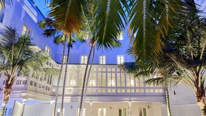 Um hotel com vários andares, varanda, palmeiras e uma entrada bem iluminada.