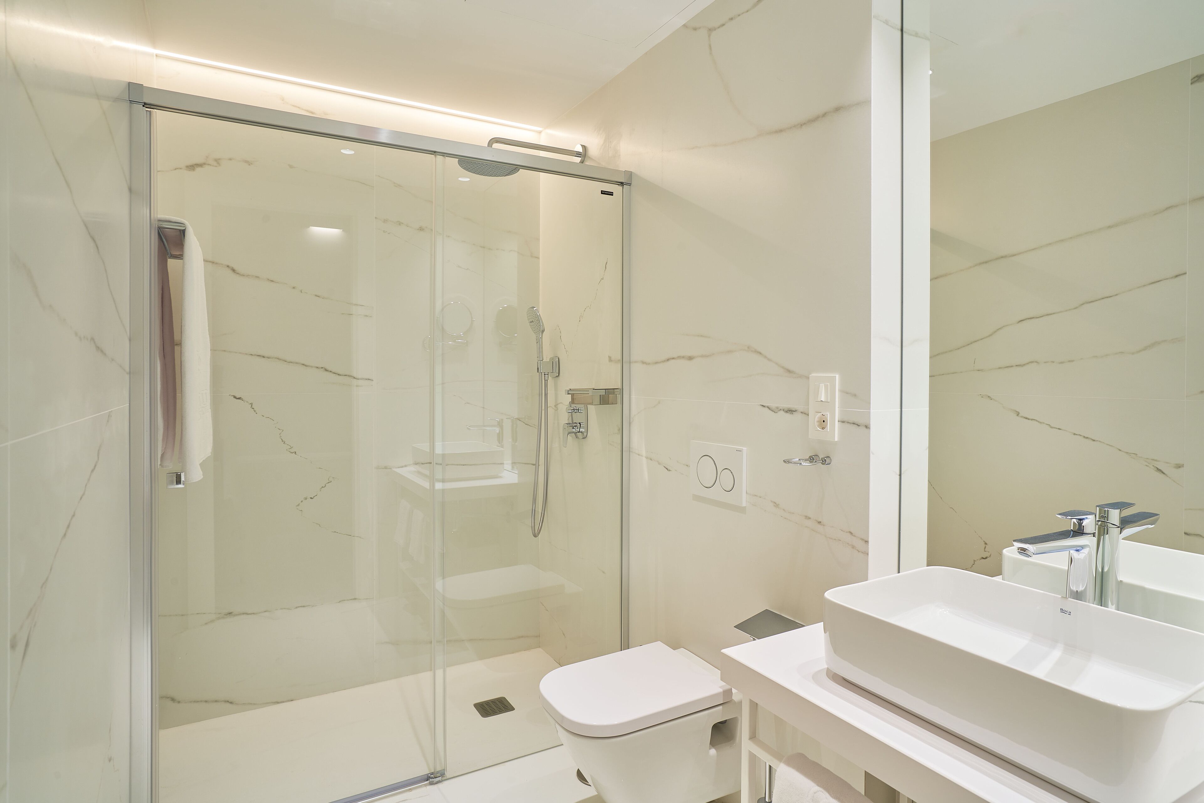 Ein modernes Badezimmer mit einer Glaskabine zur Dusche, einem weißen Waschbecken und einer Toilette.
