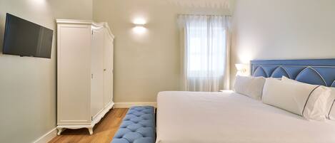 Een slaapkamer met een bed, een bankje, een kledingkast en een televisie aan de muur.
