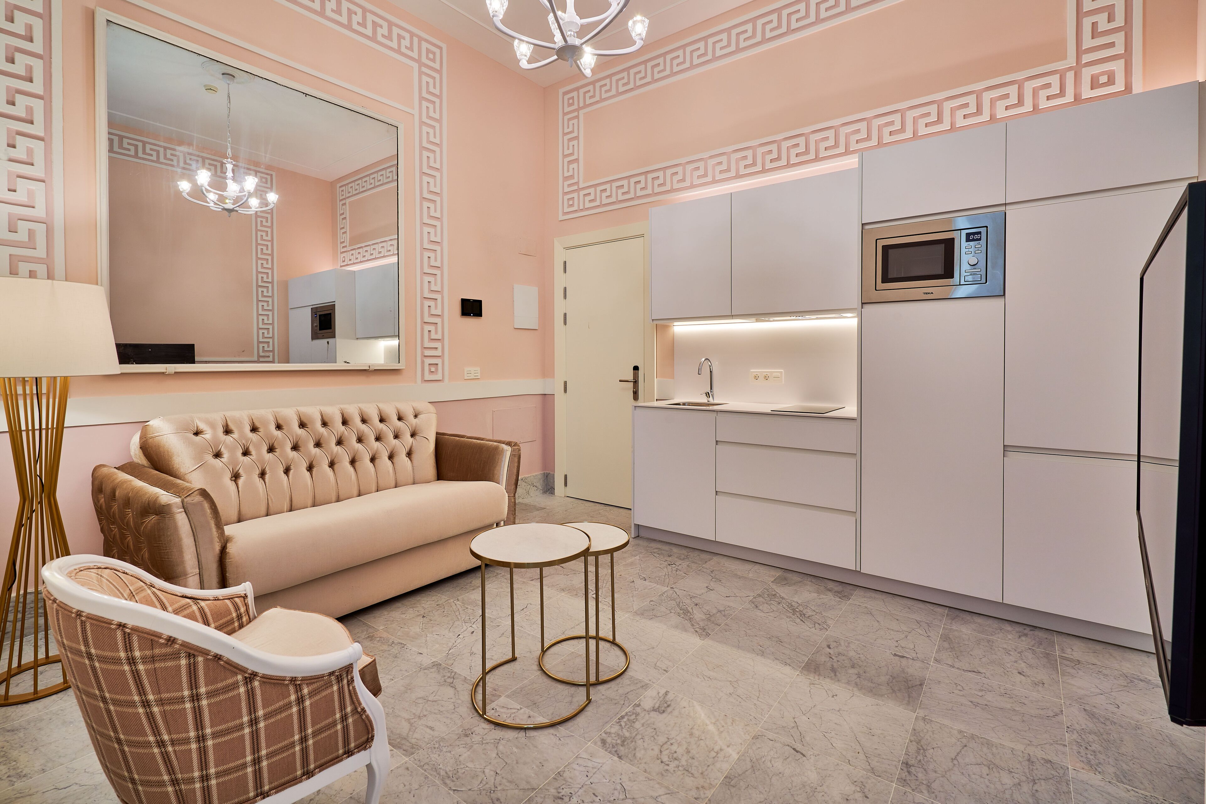 A modern living room with a sofa, two side tables, a chandelier, and a kitchen area with a microwave.