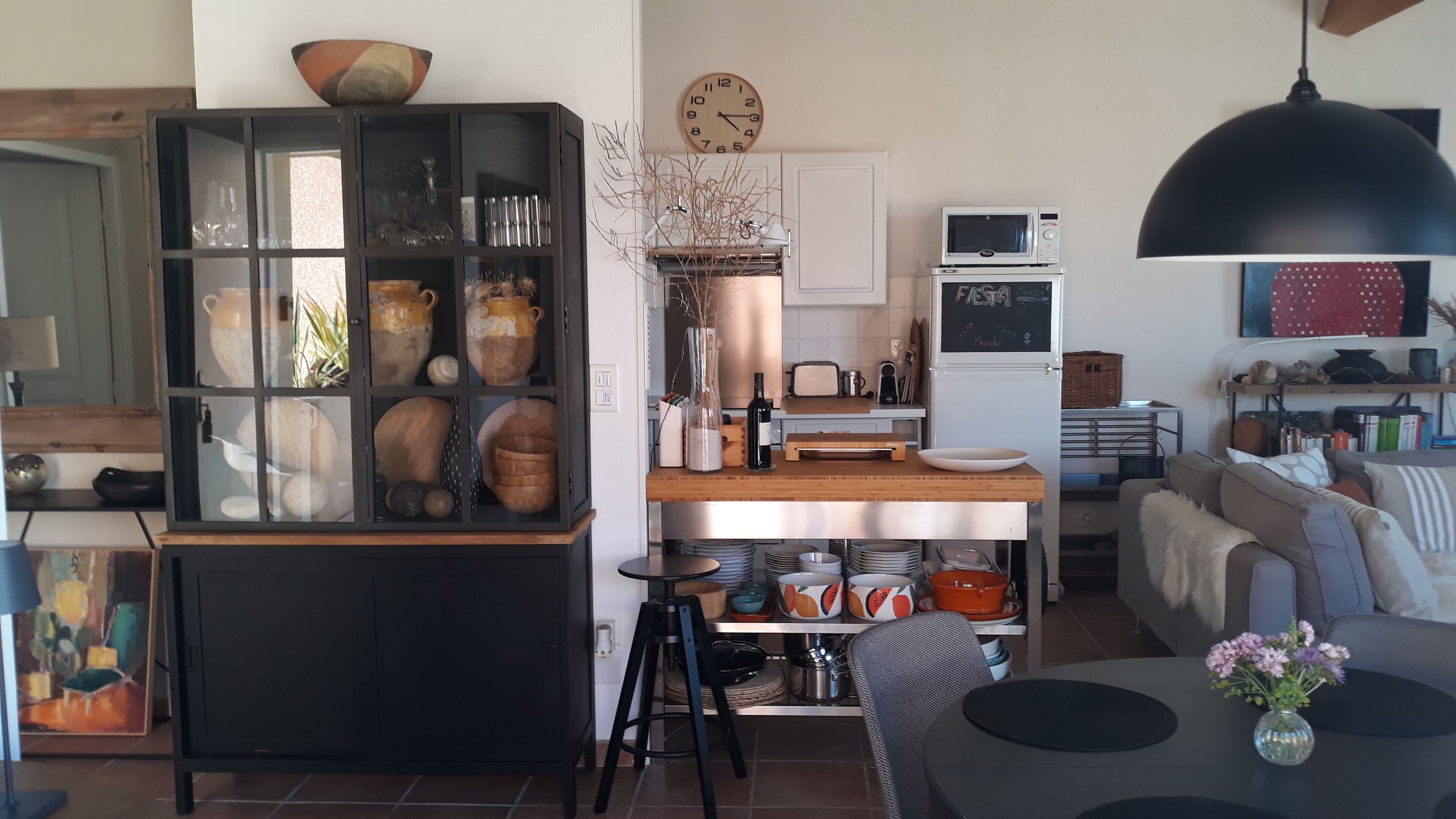 A modern kitchen with a wooden island, a black cabinet with glass doors, and a dining area with a table and chairs.