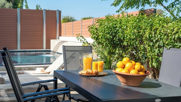 A poolside area with a table set for breakfast, including a bowl of lemons and a pitcher of orange juice.