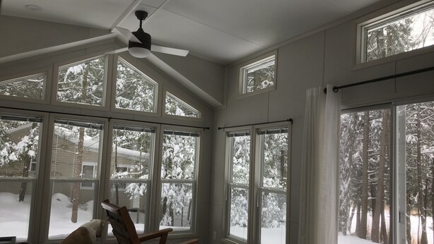 A sunroom with large windows, a ceiling fan, and a dog in a dog bed. - Park Model Single Family double lofted private heaven on a pond (Otis)