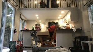 A compact kitchen with a central island, a dining area with a chair, and a pet bed. - Park Model Single Family double lofted private heaven on a pond (Otis)