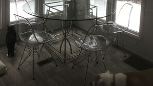 A room with a glass table surrounded by clear chairs, large windows, and a view of trees and a snowy landscape. - Park Model Single Family double lofted private heaven on a pond (Otis)