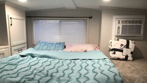 A bedroom with a bed, a window with blinds, a wall-mounted air conditioner, and a carpeted floor. - Park Model Single Family double lofted private heaven on a pond (Otis)
